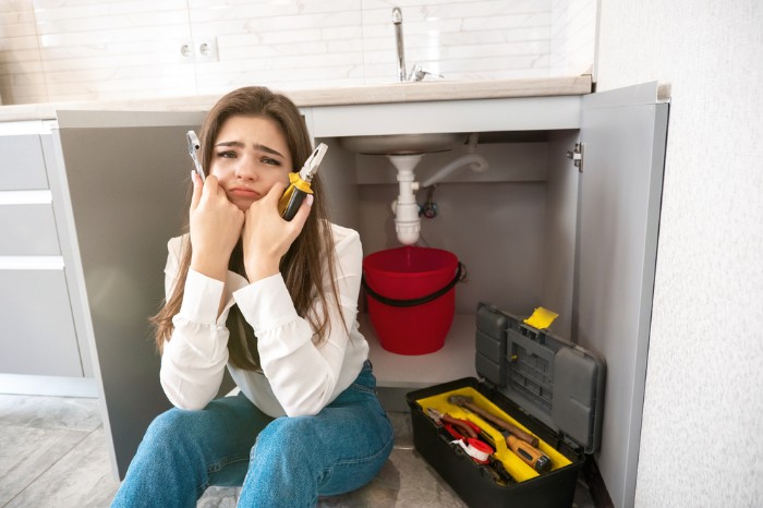 woman with a frustrated look on her face while trying to fix her kitchen drain pipe leak 